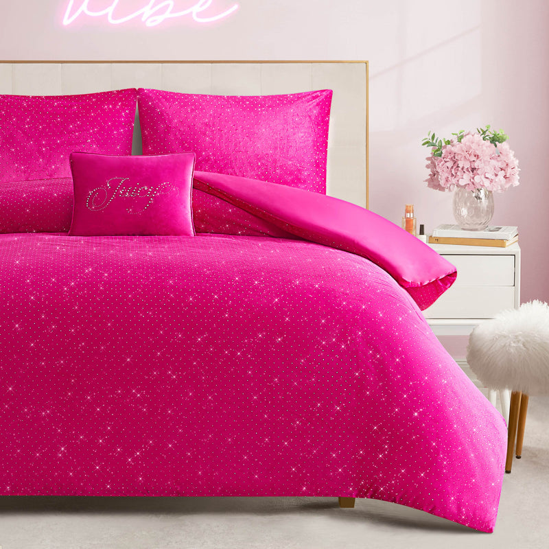 A bedroom featuring the Velvet Rhinestone Princess Comforter Set in sparkling hot pink, paired with a decorative pillow and a neon sign glowing above the bed. A nightstand displays a vase of pink flowers alongside books, while soft pink walls and a fluffy white stool complete the scene.