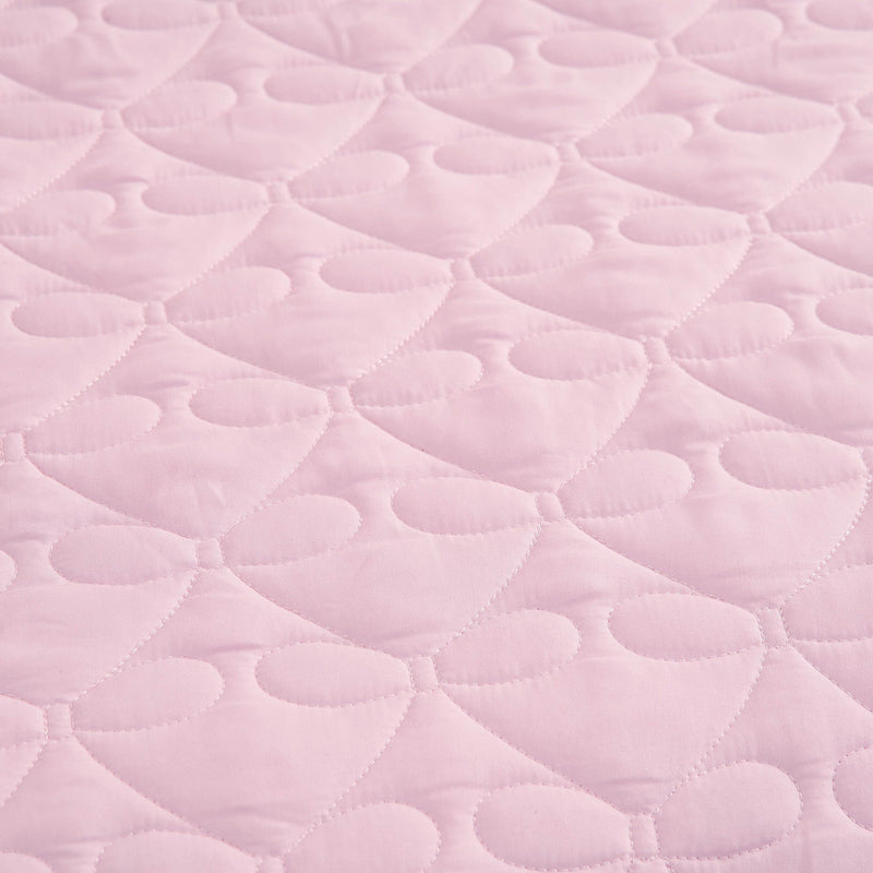 Light pink quilted fabric with a repeating pattern of stitched hearts and rounded shapes, reminiscent of the Luxe Bow Reversible Quilt Set, creates a soft, textured surface perfect for cozy microfiber comforters or bow print bedding ensembles.