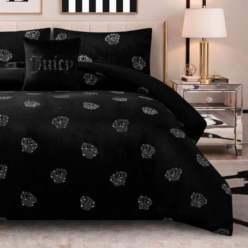 A chic bedroom featuring the Velvet Rhinestone Royal Bling Comforter Set—a black ensemble adorned with silver rhinestone crown patterns—coordinated with a Juicy accent pillow, mirrored nightstand, lamp, and framed wall art.