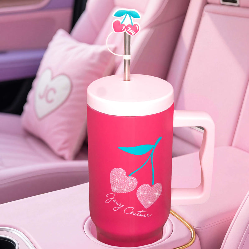 A GoGlam Rhinestone Tumbler with Handle, Straw, and Topper featuring a cherry design sparkles in a pink car interior adorned with heart pillows and JC monograms.
