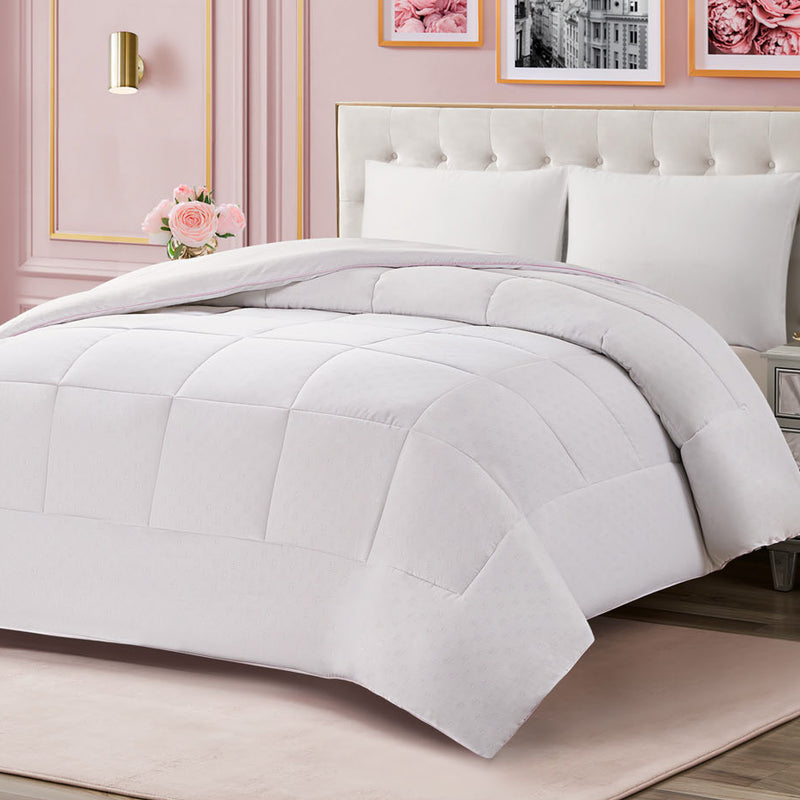 Elegant bedroom featuring a white tufted bed adorned with the Embossed J Down Alternative Comforter and matching pillows. Pink flowers and framed art hang on pink walls, while a vase of roses rests on the bedside table.