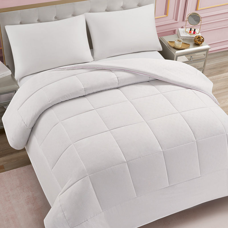 A neatly made bed featuring the Embossed J Down Alternative Comforter, white pillows, and a tufted headboard. Nightstands with lamps and decor sit on either side, complemented by a pink wall and wooden floor.