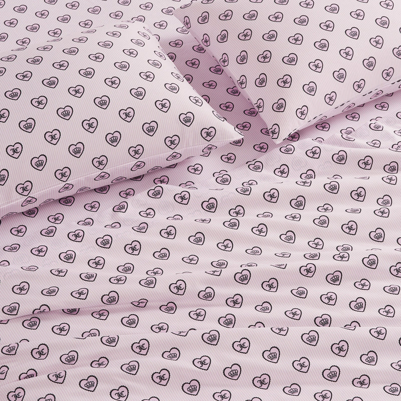 Printed Microfiber Sheet Set in pink, featuring a repeating pattern of outlined black hearts with small faces inside. Two pillows sit at the top of the neatly made bed, adding a playful twist to this luxe bedding set.