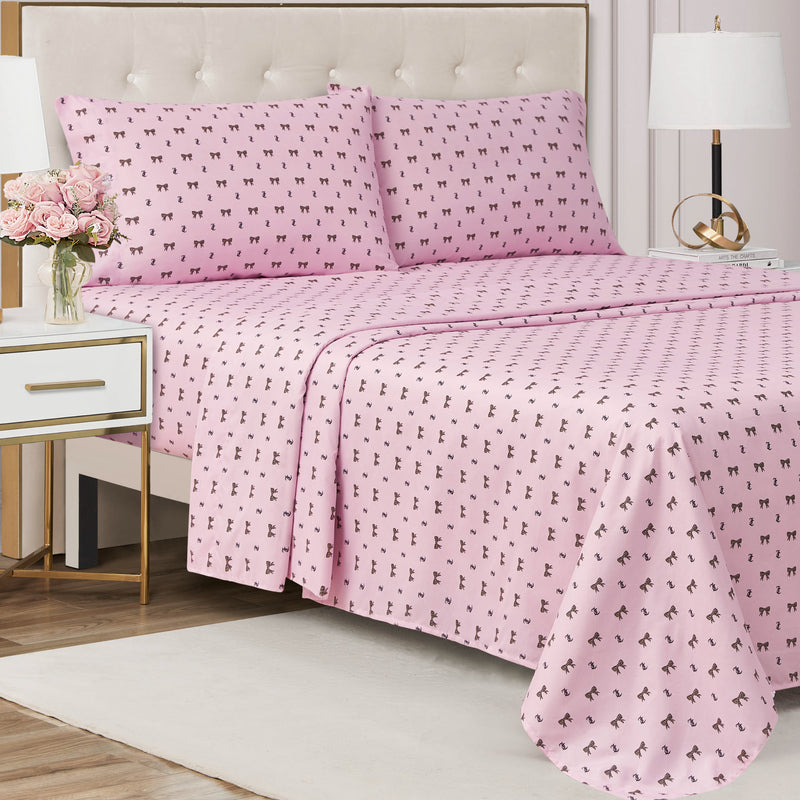 A neatly made bed with the Printed Microfiber Sheet Set in pink, featuring pillowcases adorned with a small black dog pattern, placed next to a white nightstand holding a vase of pink flowers and a lamp, in a bright, modern bedroom.