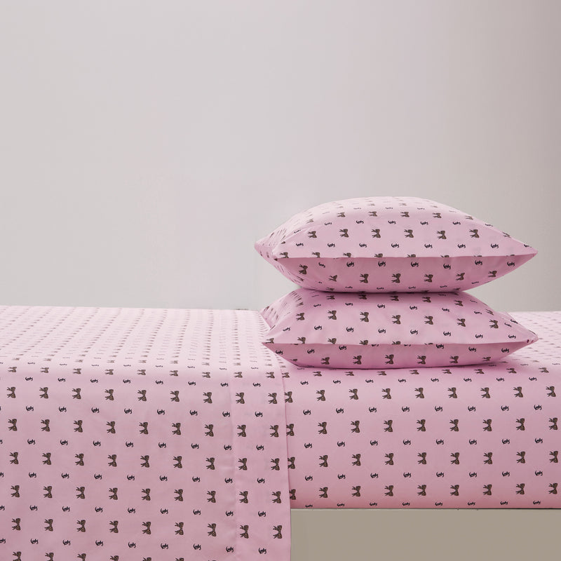 The Printed Microfiber Sheet Set, featuring pink bed sheets and two stacked pillows adorned with a small repeating black floral pattern, is neatly arranged on a simple bed against a plain, light-colored wall to create an inviting look reminiscent of luxury bedding.