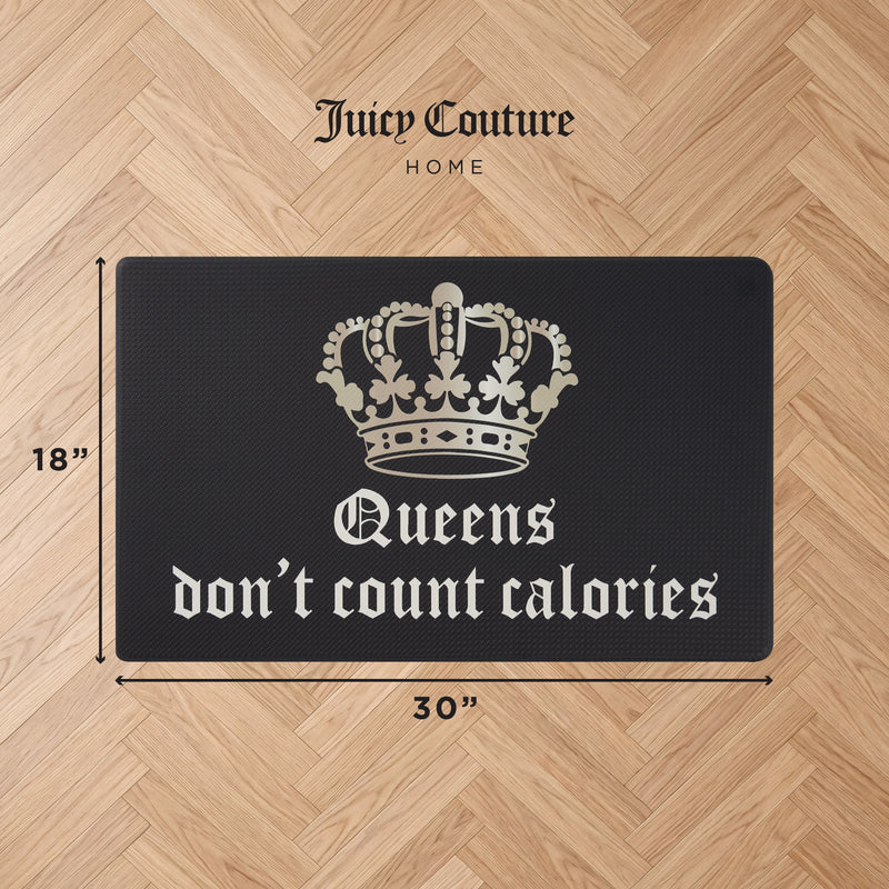 A black Kitchen Wellness Mat by Juicy Couture, featuring a white crown graphic and the phrase “Queens don’t count calories,” measures 18 inches by 30 inches and adds chic, cushioned anti-fatigue support on a light wood floor.