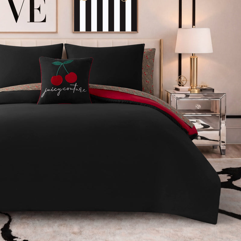 A neatly made bed with the Cherry Toss Cheetah Solid Reversible Comforter Bed in a Bag bedding set, a cherry-themed pillow, a mirrored nightstand with a lamp, and minimalist wall art above the headboard.