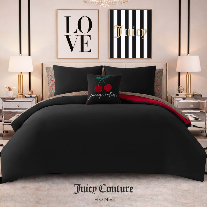 A stylish bedroom featuring the Cherry Toss Cheetah Solid Reversible Comforter Bed in a Bag Bedding Set in black, accented with a cherry-themed pillow, two bedside tables with lamps, and framed LOVE and Juicy prints above the bed. The chic comforter adds a playful touch of cherry and cheetah pattern, while “Juicy Couture Home” is written at the bottom.