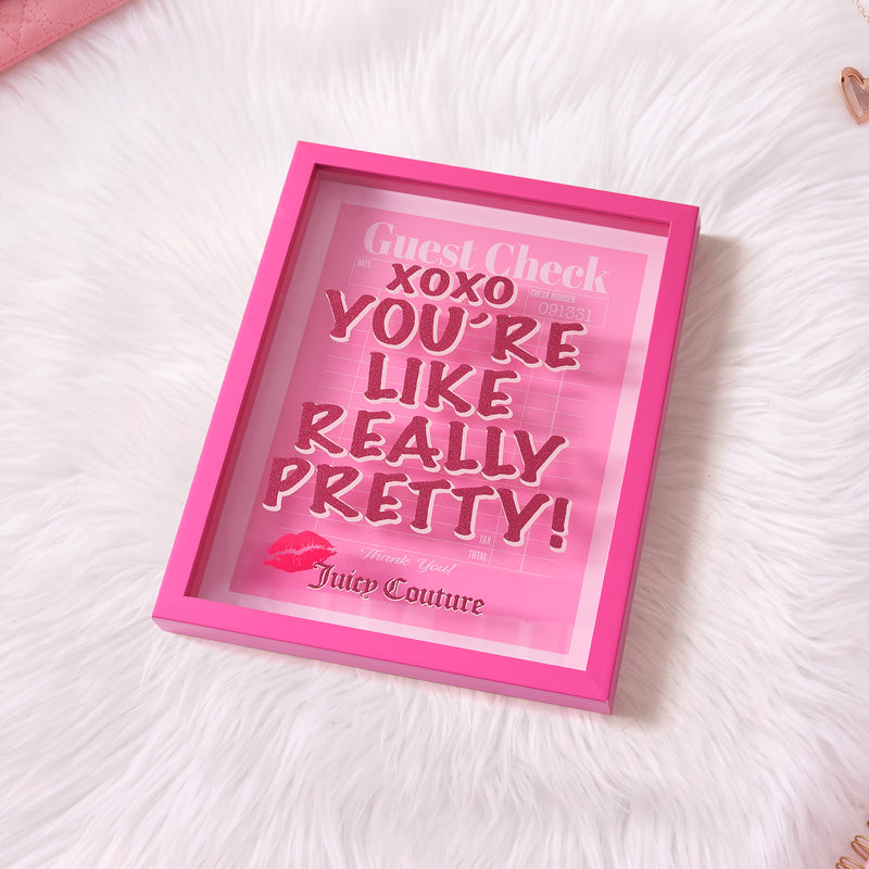 The Shadow Box Wall Art, 12″ x 16″, features a pink-framed sign set against white faux fur, displaying “Guest Check XOXO YOU’RE LIKE REALLY PRETTY! Juicy Couture” in stylish fonts with pink lipstick marks—creating a chic, fashion-inspired accent reminiscent of a Juicy Couture shadow box.