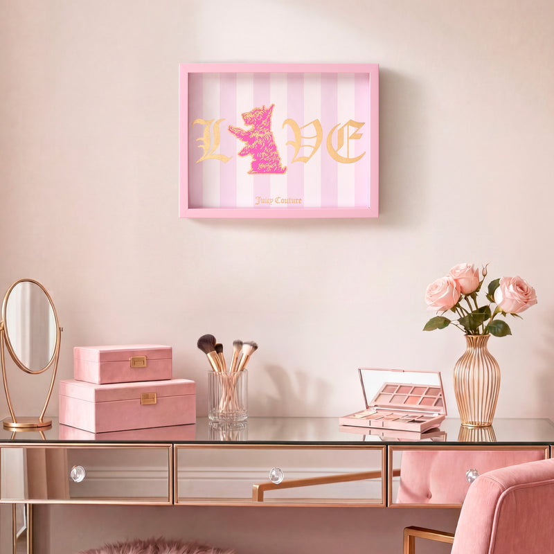 A pink-themed vanity adorned with makeup items and roses, showcasing the Shadow Box Wall Art (12″ x 16″) on the wall—a chic statement piece featuring “LOVE” in gold letters with a pink dog silhouette and “Juicy Couture” beneath, offering a fashion-inspired touch to the space.