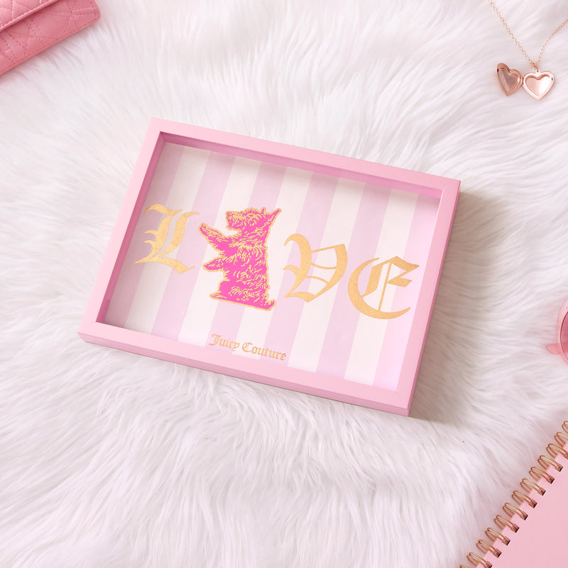 A pink Juicy Couture Shadow Box Wall Art (12″ x 16″) featuring gold LOVE text and a lion, displayed on white fur alongside heart jewelry, a pink wallet, and a spiral notebook—perfect for showcasing your favorite fashion-inspired artwork or adding stylish decor to your space.