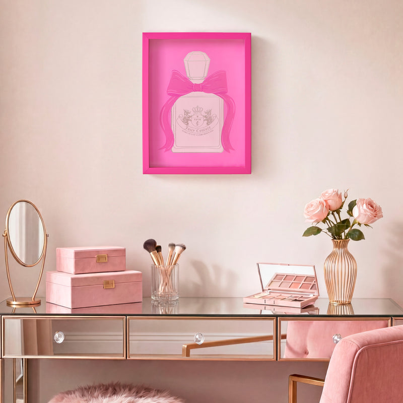 A chic vanity with a glass top, makeup items, pink velvet boxes, a vase of pink roses, and a framed “Shadow Box Wall Art, 12\” x 16\“” featuring a pink bow displayed on the pale pink wall above.