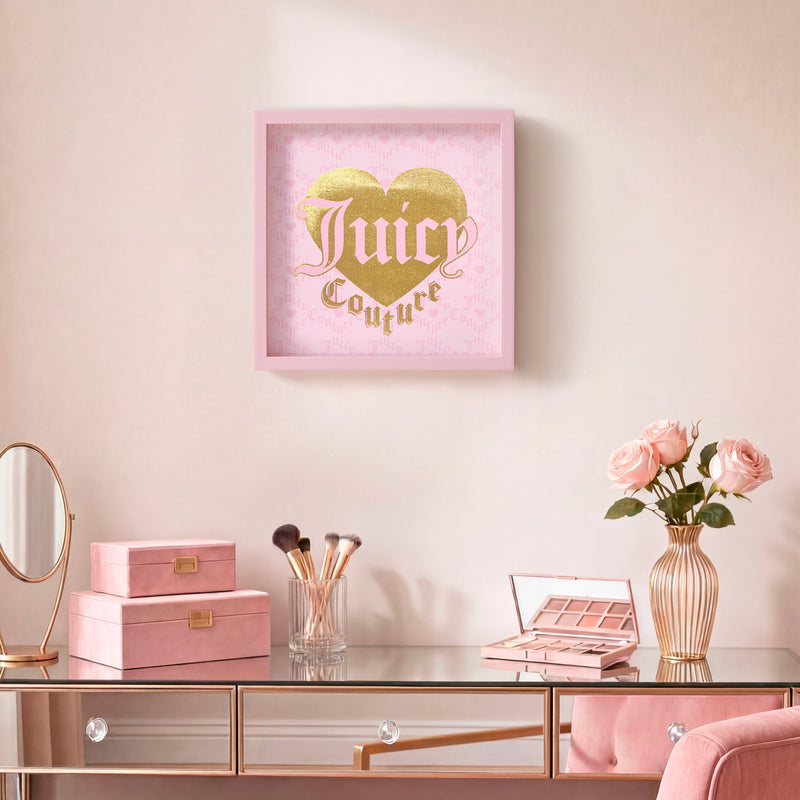 A pink vanity with makeup, brushes, and roses sits below a framed Shadow Box Wall Art, 14″ x 14″, featuring a gold and pink heart print on a pale pink wall.