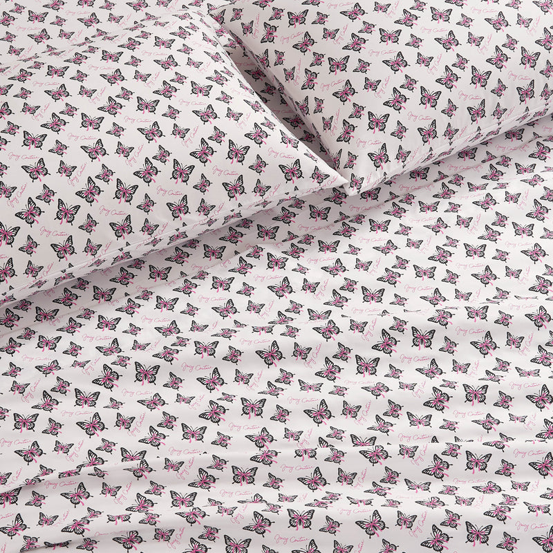 Two bed pillows and a flat sheet in a Printed Microfiber Sheet Set featuring a repeating pattern of pink and black butterflies on a white background.