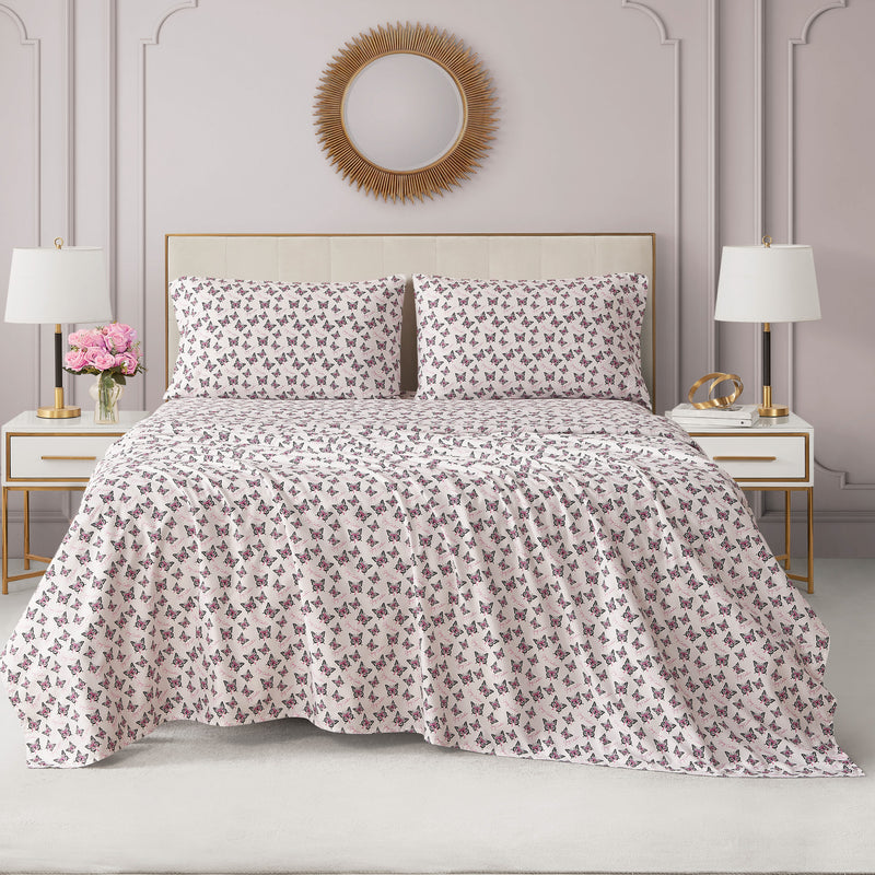 Bed made with a Printed Microfiber Sheet Set featuring light-colored Juicy Couture sheets and pillowcases with a pink and black butterfly pattern.