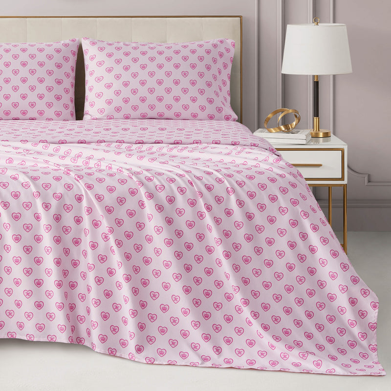 Bed covered in a Printed Microfiber Sheet Set by Juicy Couture featuring pink sheets patterned with small red hearts and crowns.