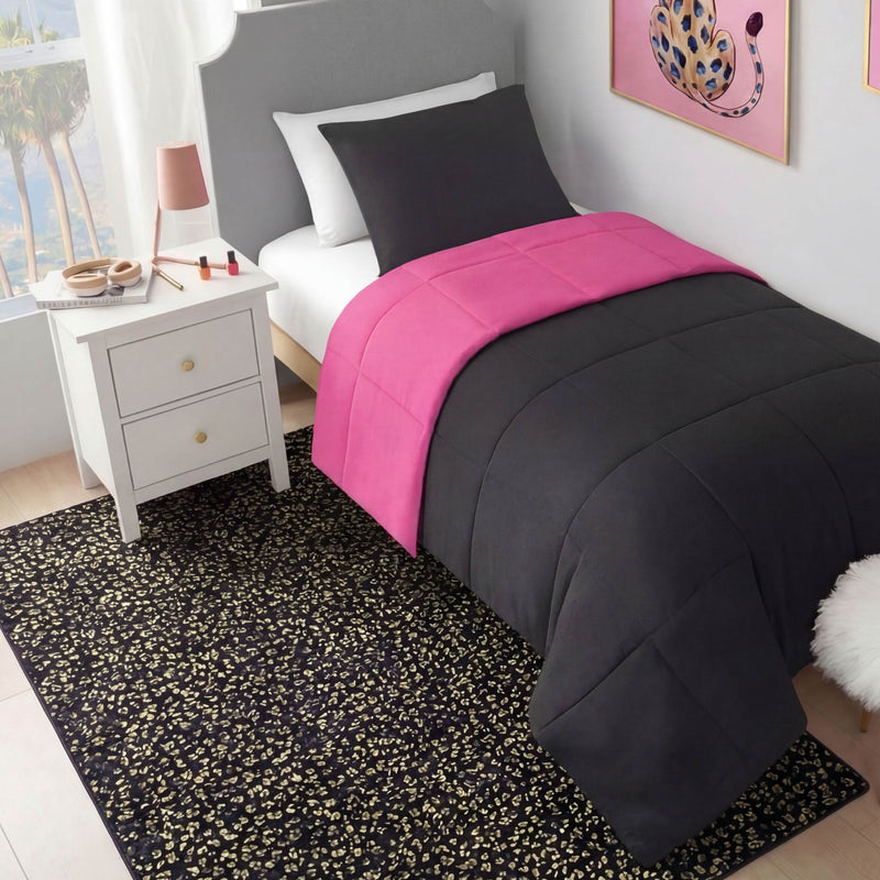 A neatly made twin bed with black and hot pink bedding sits by a white nightstand with drawers. A Metallic Leopard Plush Rug, 4' x 6', covers the floor, while colorful artwork brightens the pale wall.