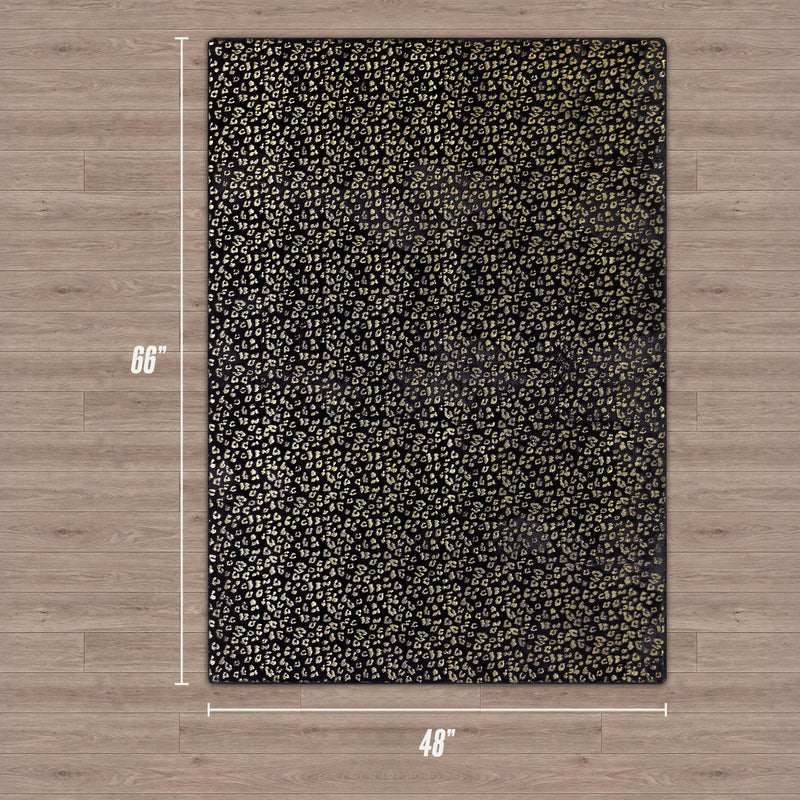 The Metallic Leopard Plush Rug, 4' x 6', features a black background with a gold metallic leopard print pattern and is shown on a light wood floor.