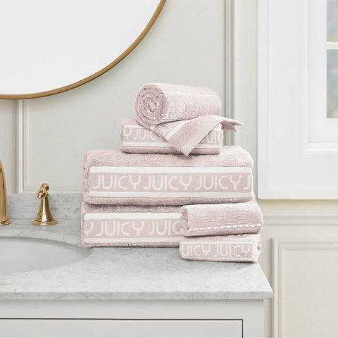 A stack of folded Plush Stripe Bath Towel Set towels rests on a marble bathroom counter beside a gold faucet and round mirror, with a window in the background.
