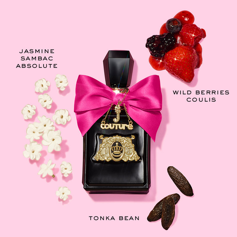 A black Viva La Juicy Elixir Eau de Parfum Spray bottle with a pink bow and gold charm is surrounded by jasmine flowers, wild berries coulis, and tonka beans on a pink background—highlighting its iconic women’s fragrance notes.