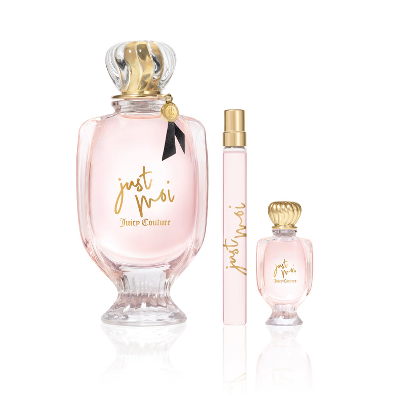 The Just Moi 3 Piece Fragrance Gift Set by Juicy Couture features a large bottle adorned with a gold-crowned lid, a tall and slim Eau de Parfum spray, and a small bottle with a gold lid. Each bottle contains light pink liquid and is detailed with elegant gold writing on white, beautifully embodying the feminine allure of this fragrance collection.