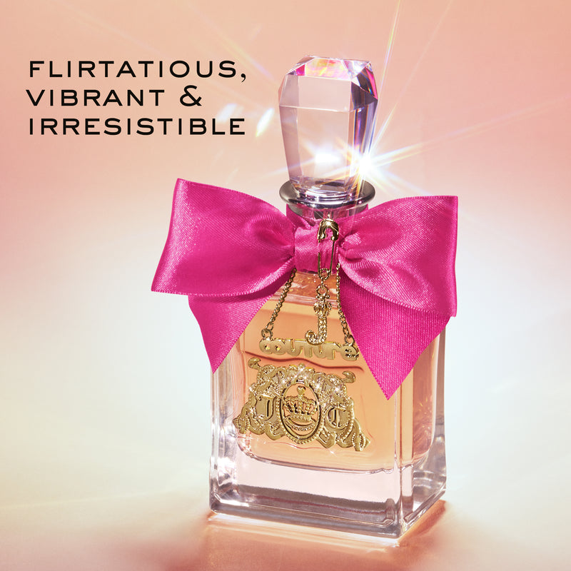 A perfume bottle with a faceted cap, a bright pink bow, and gold detailing sits on a pink background. Text reads: Flirtatious, Vibrant & Irresistible. Experience the playful spirit of the Viva La Juicy Le Bubbly 3 Piece Fragrance Gift Set from Juicy Couture.