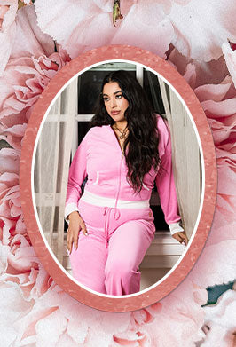 Woman in pink outfit standing in front of a mirror with floral decorations.