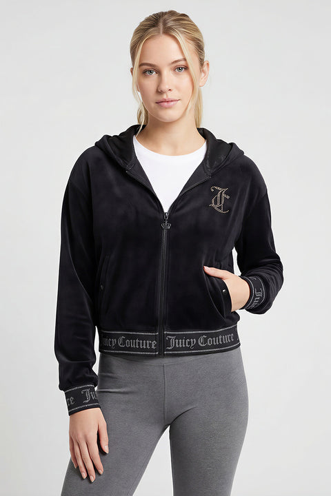 A woman wears the black Reversible Velour Jacket with logo trim on the cuffs and waistband over a white top and gray leggings, standing against a plain light background for an authentic Y2K style look.