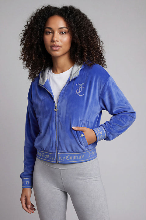 A woman with curly hair wears a blue Reversible Velour Jacket and gray leggings, channeling Y2K style as she stands against a plain light gray background.