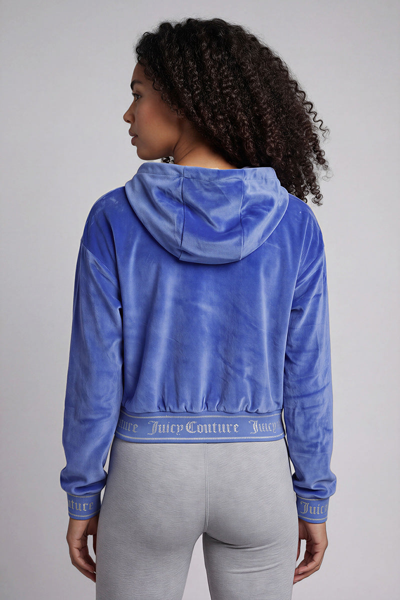A woman with curly hair, facing away, wears the Reversible Velour Jacket in blue with Juicy Couture on the waistband and cuffs, styled with light gray leggings for a trendy Y2K look.