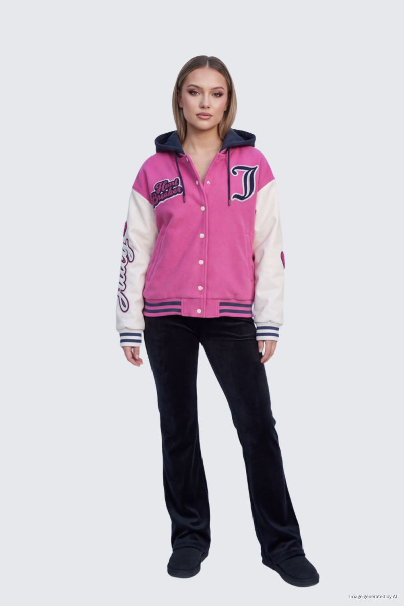 A person wearing a pink Varsity Jacket with white sleeves, a cozy fleece hood, and letter and script embroidery, paired with black flared pants.