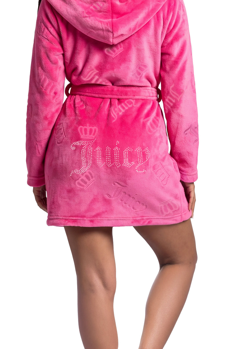 A person wearing a hot pink Hooded Luxe Plush Robe, featuring an embossed pattern and the word Juicy written in rhinestones on the back.