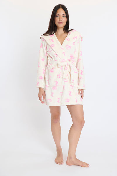 A woman stands barefoot, facing forward in a cream Hooded Luxe Plush Robe with a pink crown pattern. The knee-length, long-sleeved robe is tied at the waist. She poses against a plain white background.
