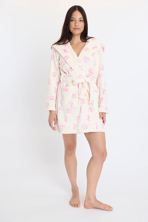 A woman stands barefoot, facing forward in a cream Hooded Luxe Plush Robe with a pink crown pattern. The knee-length, long-sleeved robe is tied at the waist. She poses against a plain white background.
