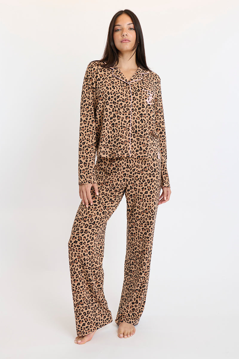 A person stands barefoot against a plain white background wearing the Plush 3-Piece PJ Set, featuring a matching long-sleeve button-down shirt and elastic waist pants with a brown and black leopard print pattern.