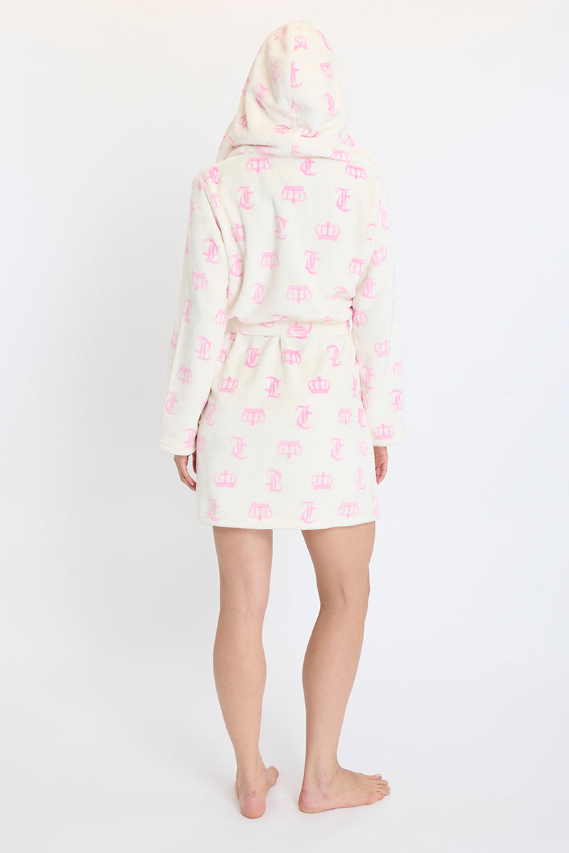 A person stands barefoot facing away, wrapped in the Hooded Luxe Plush Robe featuring pink crowns and letters, against a plain white background.
