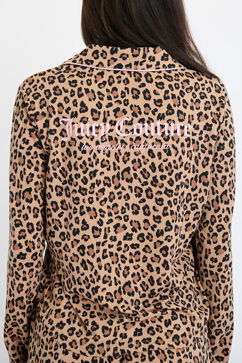 A person with long brown hair, facing away from the camera, wears the Plush 3-Piece PJ Set featuring a tan and black leopard print button-down top with "Juicy Couture" and smaller script in white lettering printed on the back.