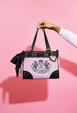 Handbag with Juicy Couture logo held by a hand against a pink background