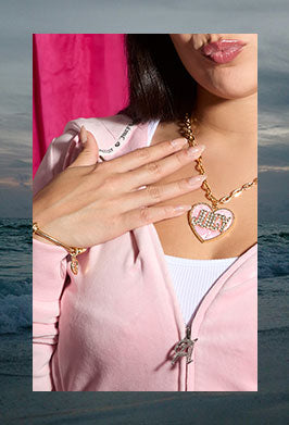 Person wearing a pink jacket with a heart necklace and gold bracelet, framed in an image of a dark beach