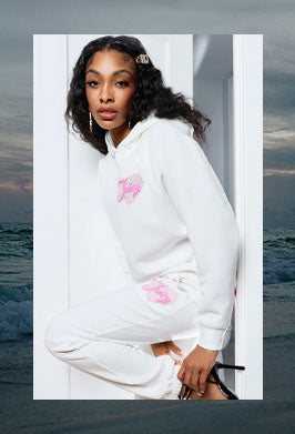 Woman wearing a white hoodie with pink graphics framed in an image of a dark beach
