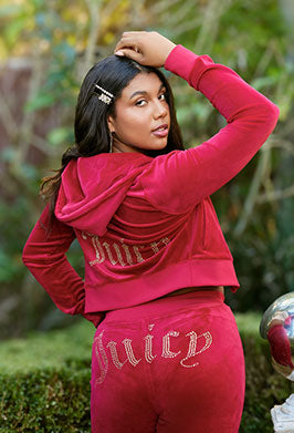 Person wearing a red 'Juicy' tracksuit with rhinestone text, standing outdoors.