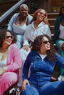 Five women in colorful tracksuits sitting on the steps of a brownstone building