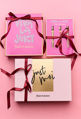 Three Juicy Couture fragrance gift boxes with ribbons on a pink background