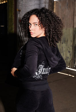 Person wearing a black tracksuit with a Juicy logo on the back in an urban setting