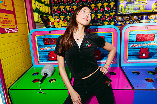 Woman in black tracksuit posing in front of a colorful Whac-A-Mole arcade game.