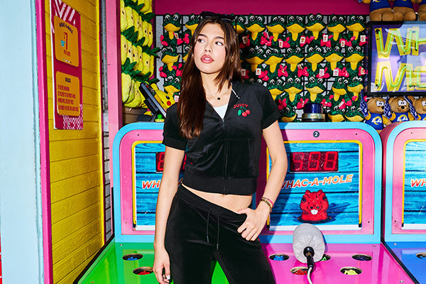 Woman in black tracksuit with a cherry print standing in front of a colorful Whac-A-Mole arcade game.