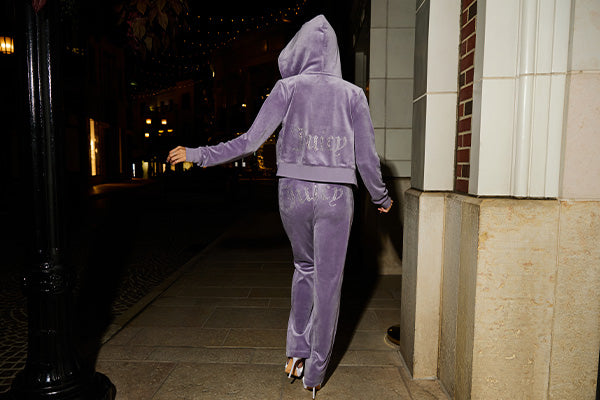 Woman in purple Juicy Couture tracksuit, her back facing the viewer, walking down the street at night