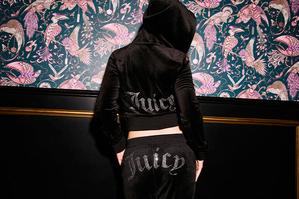 Person in black tracksuit with "Juicy" logo on the back standing against a wall