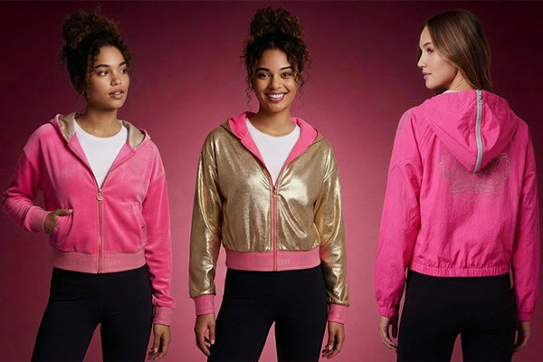 Three women model sporty hooded jackets against a pink background. The jackets are pink, gold with pink accents, and pink with a sparkly design on the back. All wear black leggings and white tops.