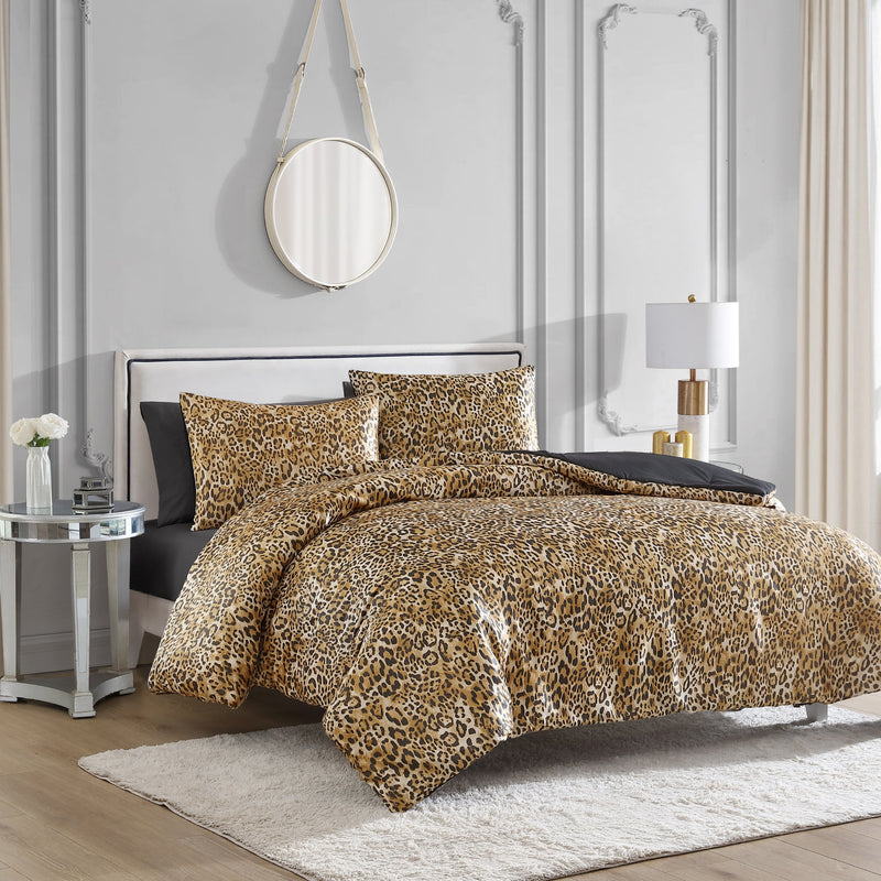 A bed with the Monica Leopard Reversible Duvet Cover Set in a modern bedroom, featuring light gray paneled walls, a round mirror, white rug, glass side table with flowers, and a chic white and gold lamp.